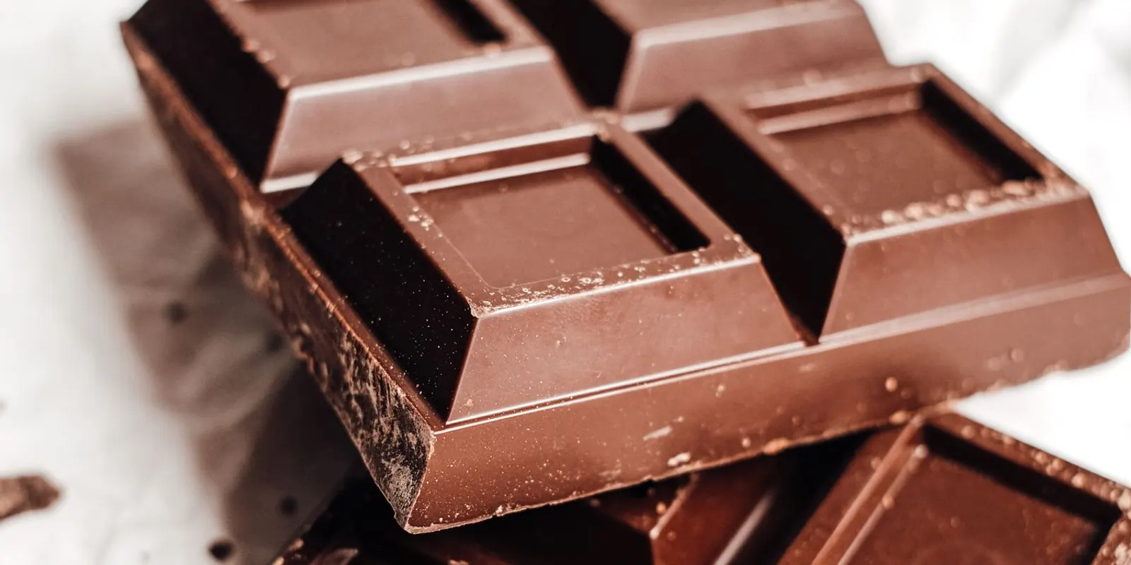 A stack of rich dark chocolate bars broken on parchment