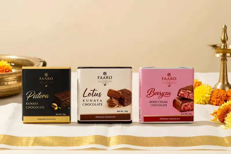 Three Faaro chocolate packs on a gold-bordered kasavu cloth beside a brass uruli of flowers and a nilavilakku lamp for Onam