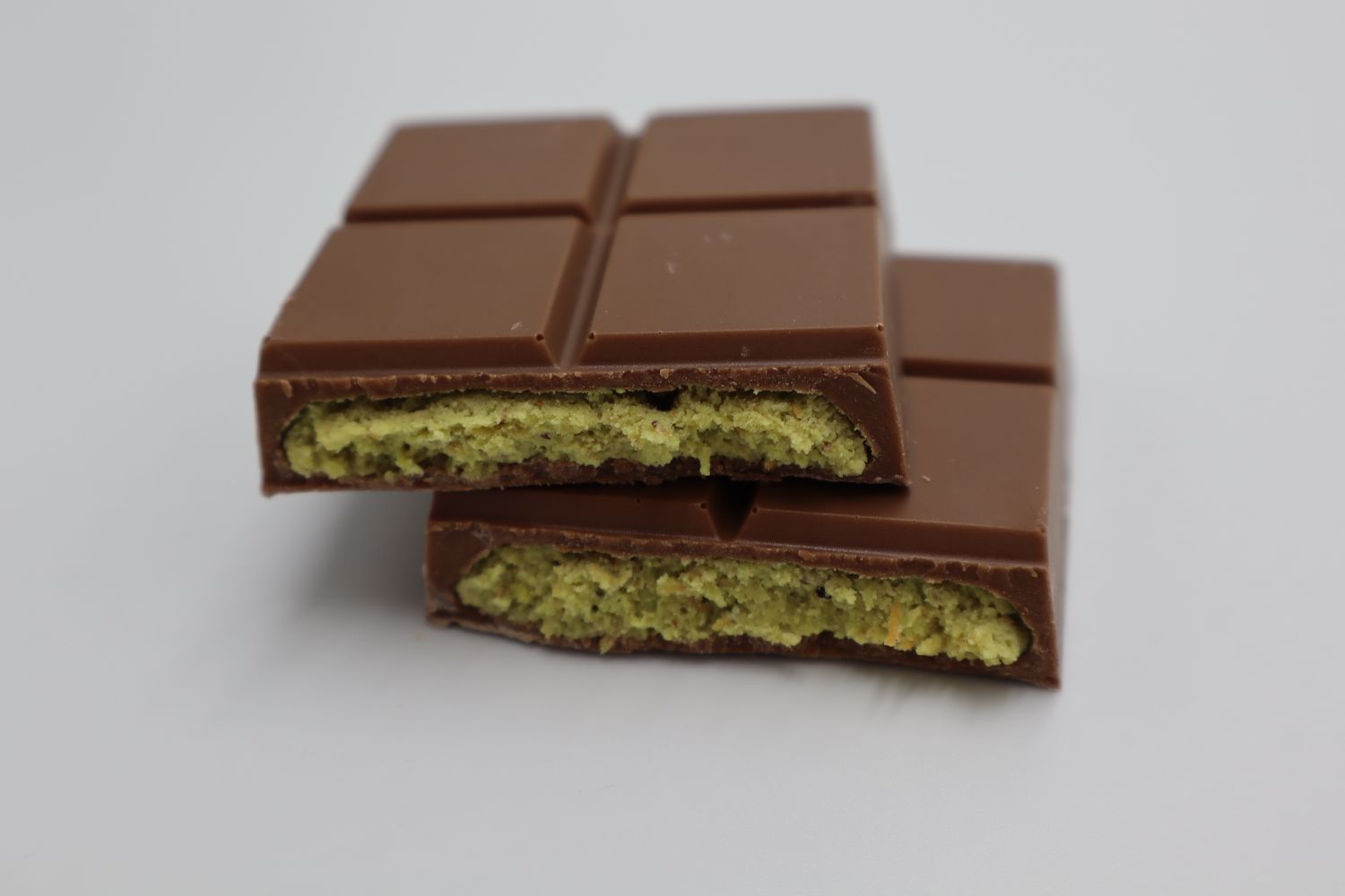 A milk chocolate bar broken open to reveal its pistachio kunafa filling