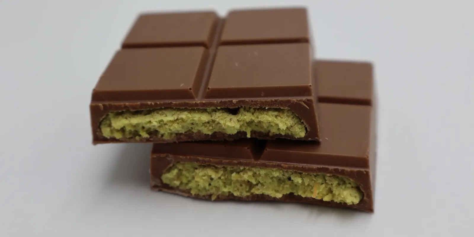 A milk chocolate bar broken open to reveal its pistachio kunafa filling