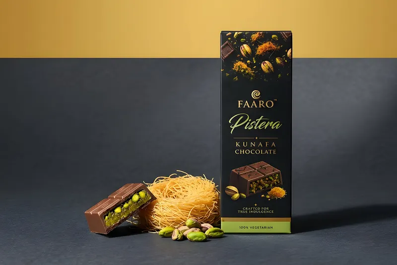 A Faaro Pistera kunafa chocolate bar beside a snapped piece showing the pistachio and kunafa filling, on a charcoal and gold backdrop