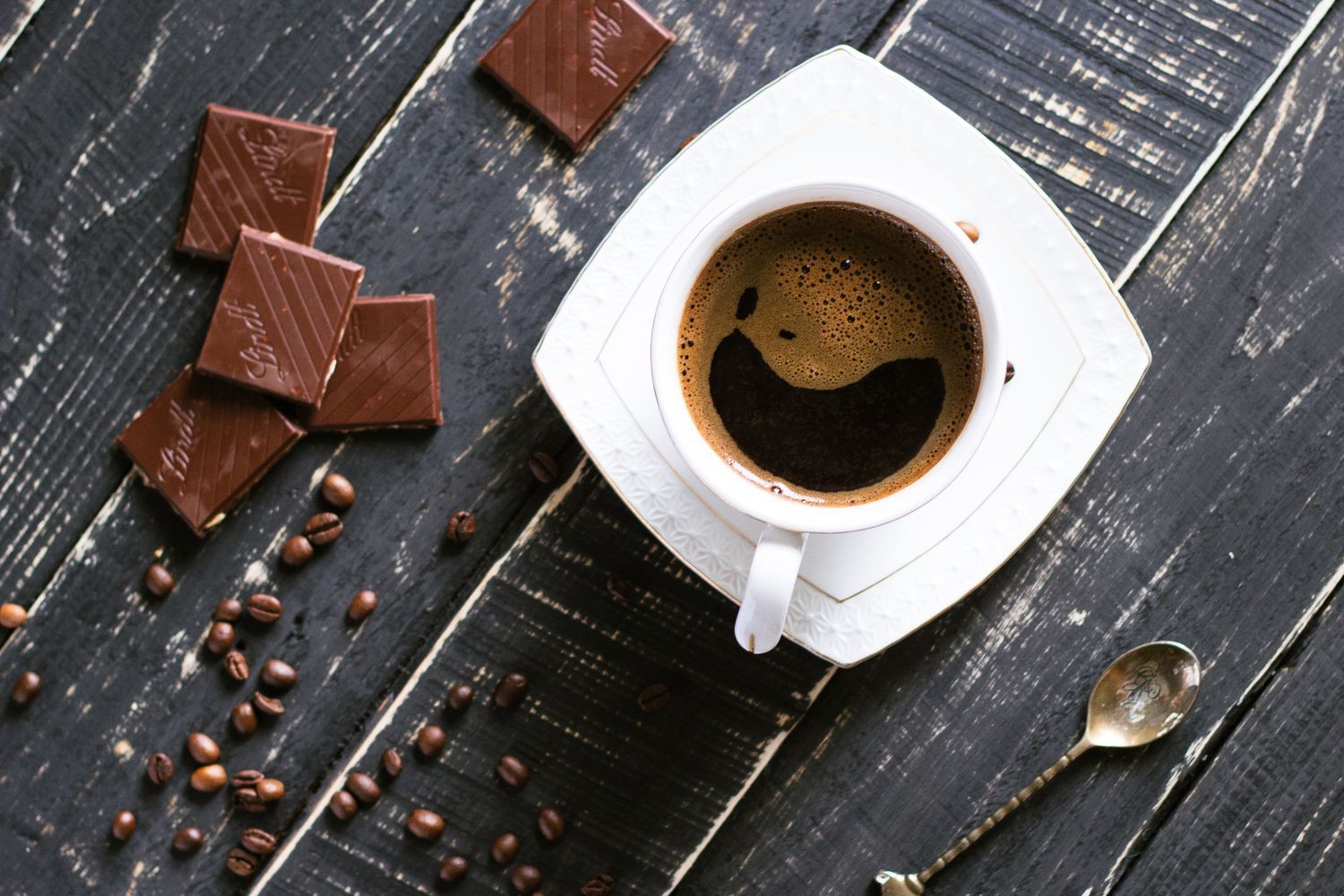 A cup of strong black coffee beside squares of chocolate and roasted coffee beans