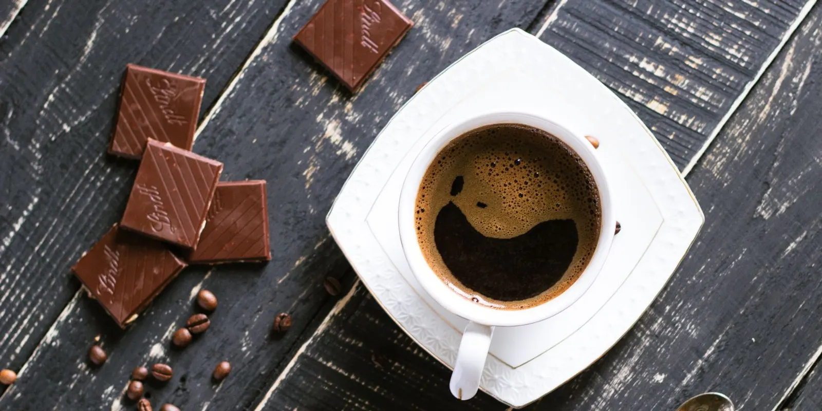 A cup of strong black coffee beside squares of chocolate and roasted coffee beans