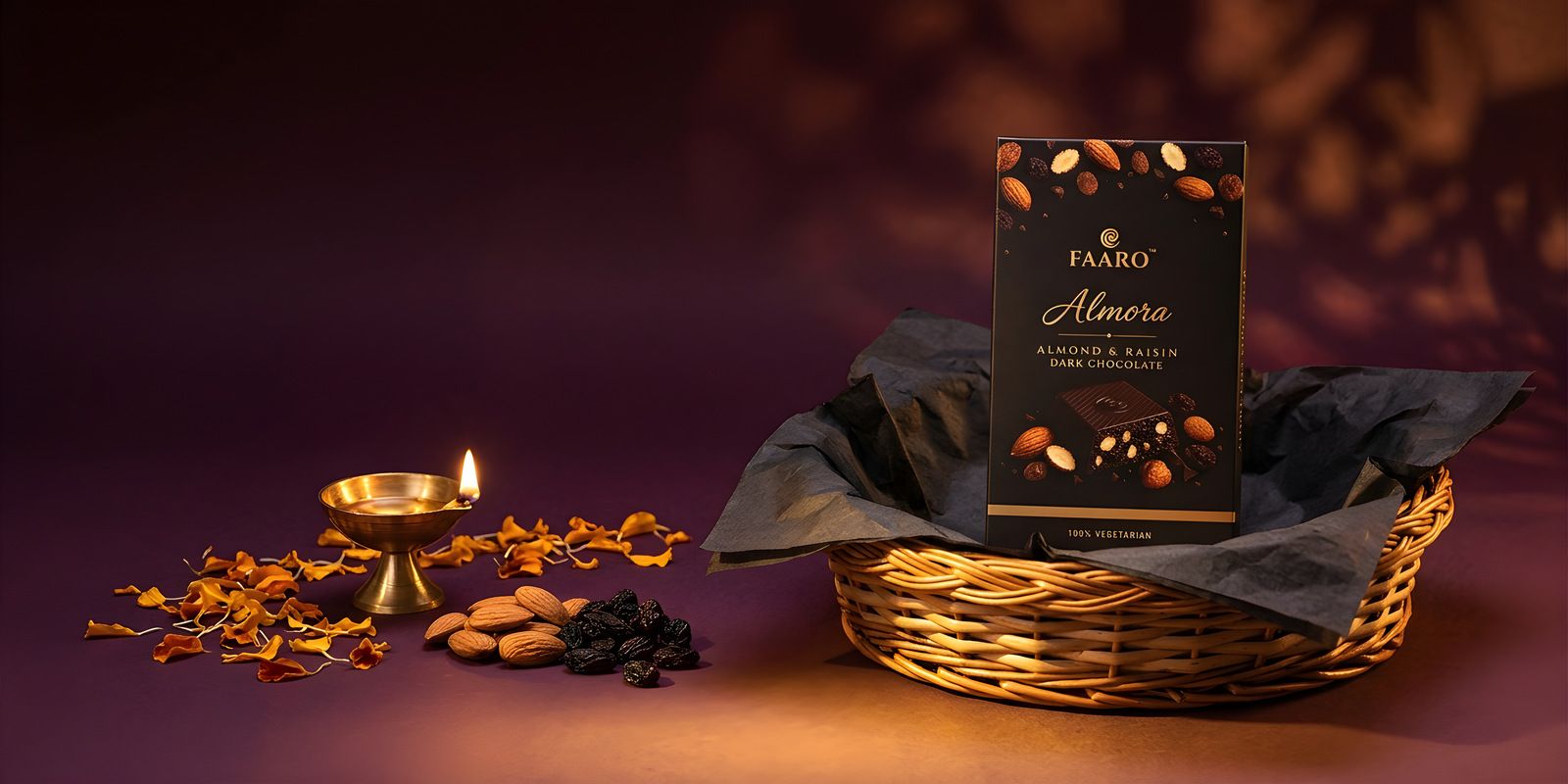A Faaro Almora dark chocolate pack in an open woven Diwali hamper with a lit brass diya, almonds and marigold petals