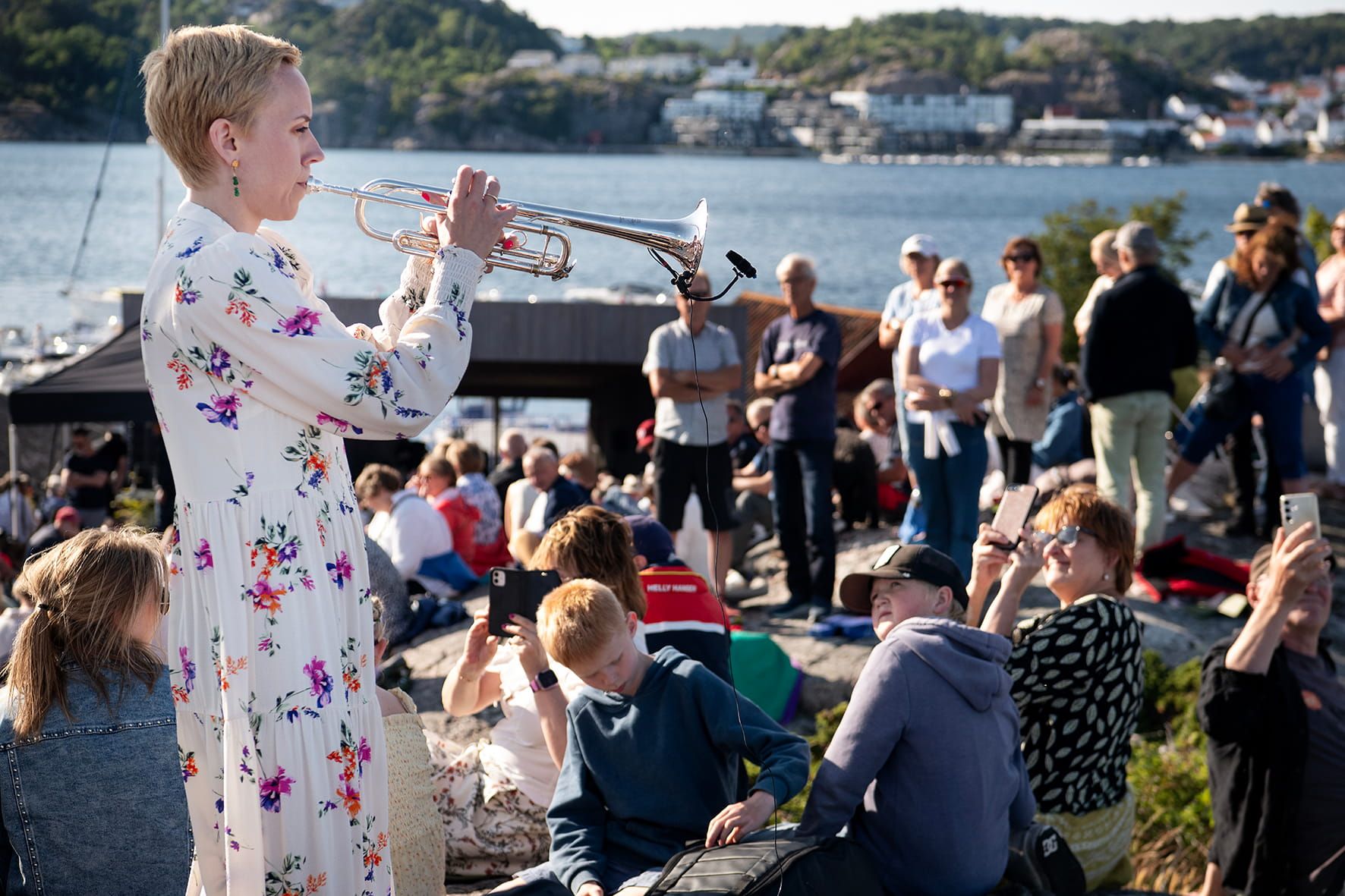 Trompetist og kunstnerisk leder Tine Thing Helseth spiller trompet foran et solfylt Stangholmen med publikum under blå himmel