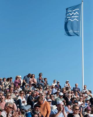 Risør kammermusikkfest sitt flagg vaier mot en blå himmel med publikum sittende i solskinnet