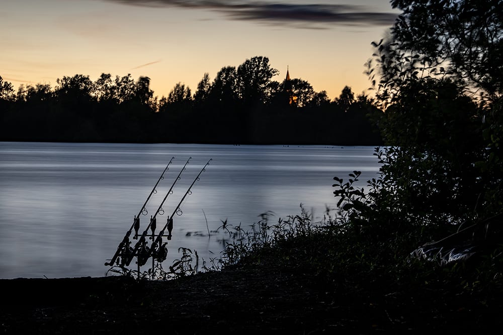 Three rods on a pod silhouetted against a lake at dusk