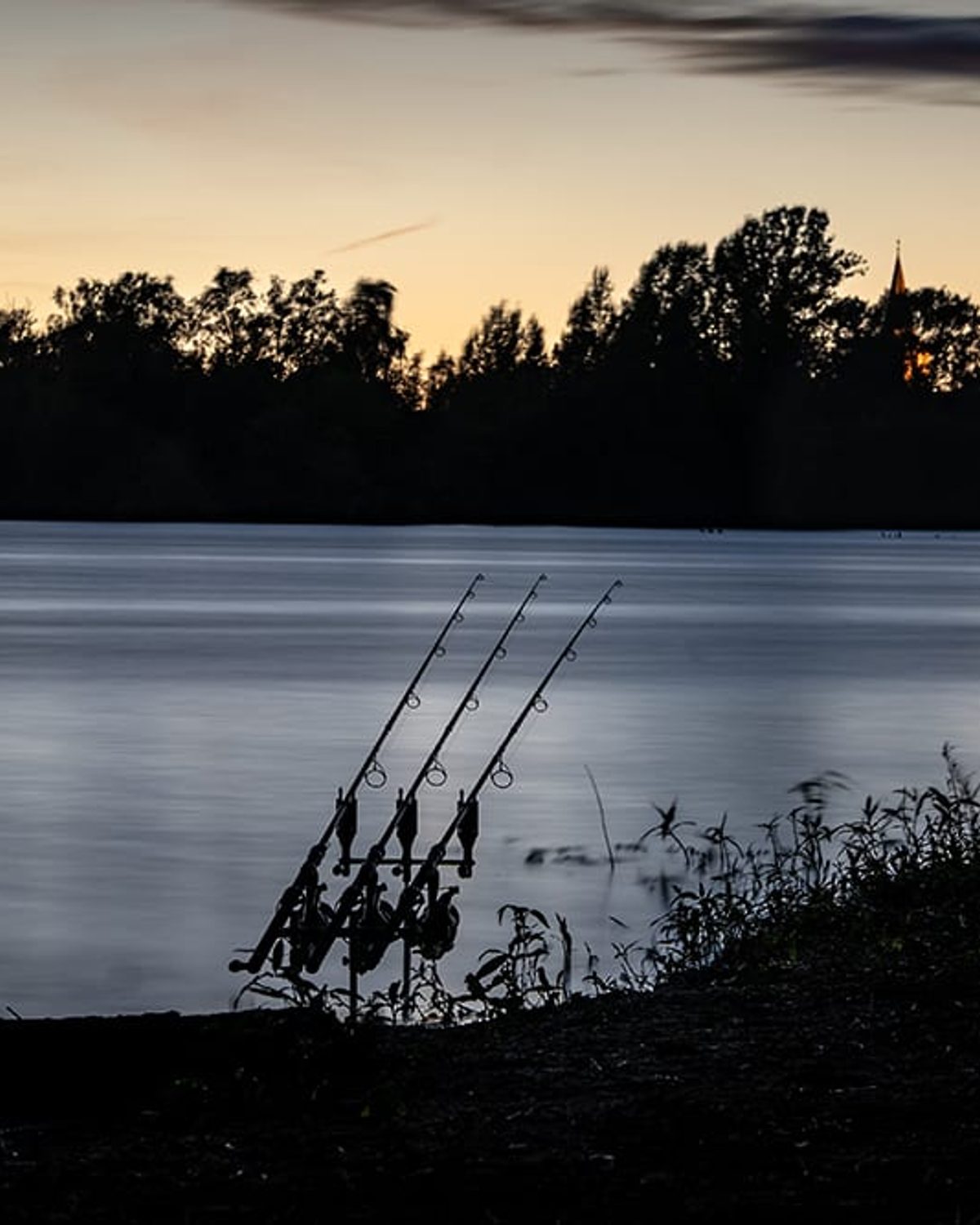 Three rods on a pod silhouetted against a lake at dusk