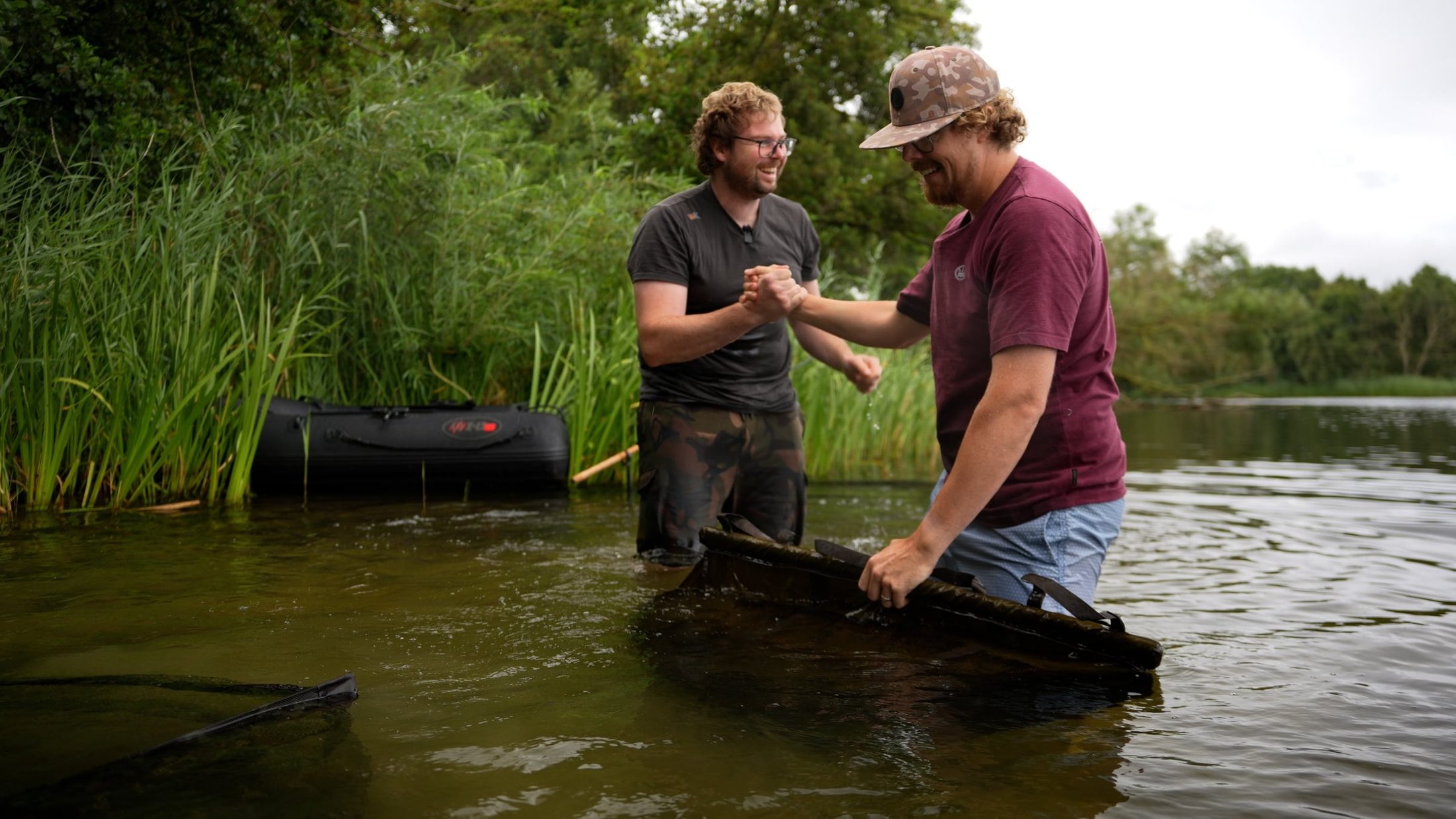 Joe shaking hands with a friend, both waist-deep in a lake beside a reed bed