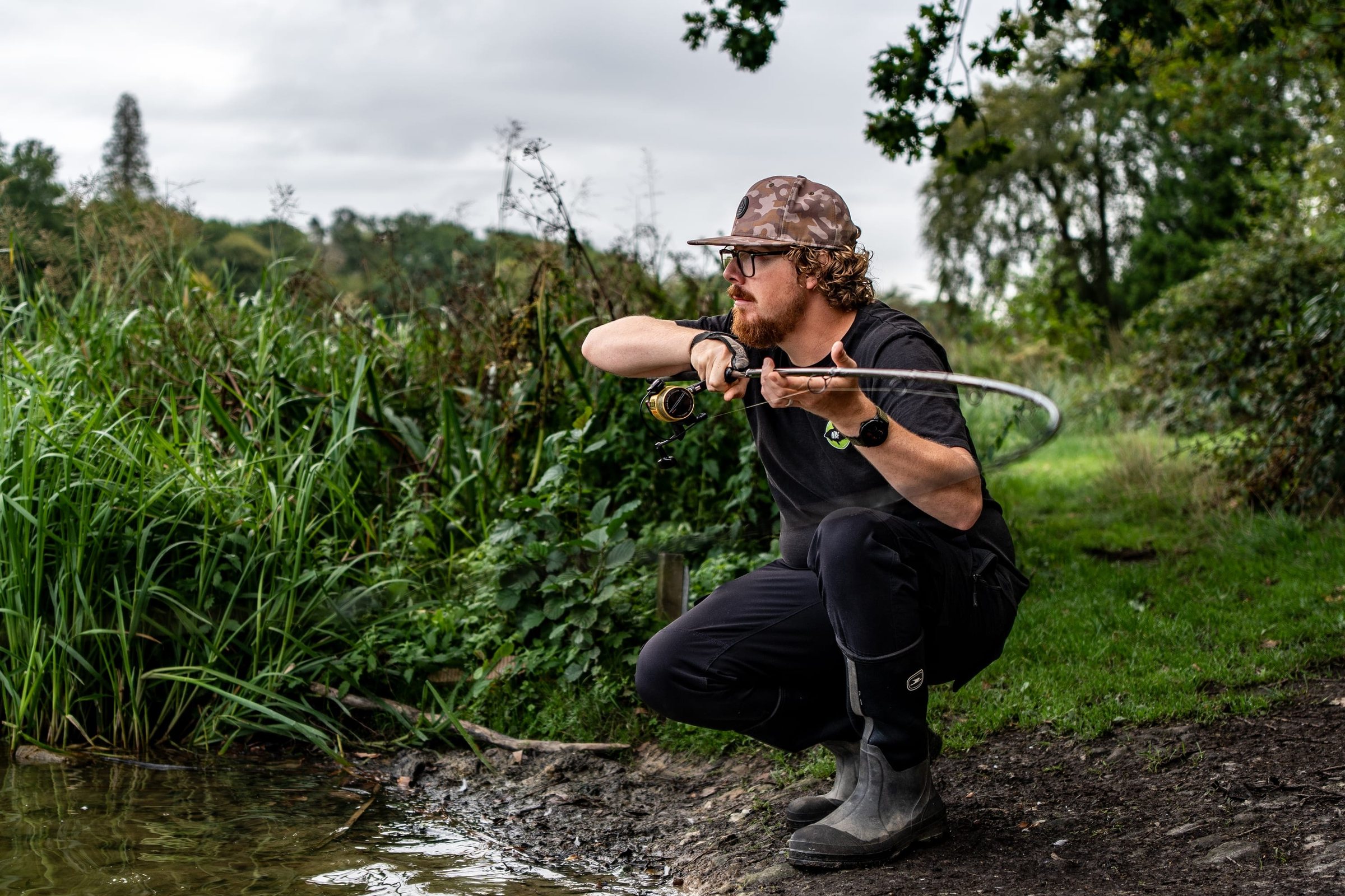 Joe crouched at the water's edge, casting a rod towards a reed-lined lake