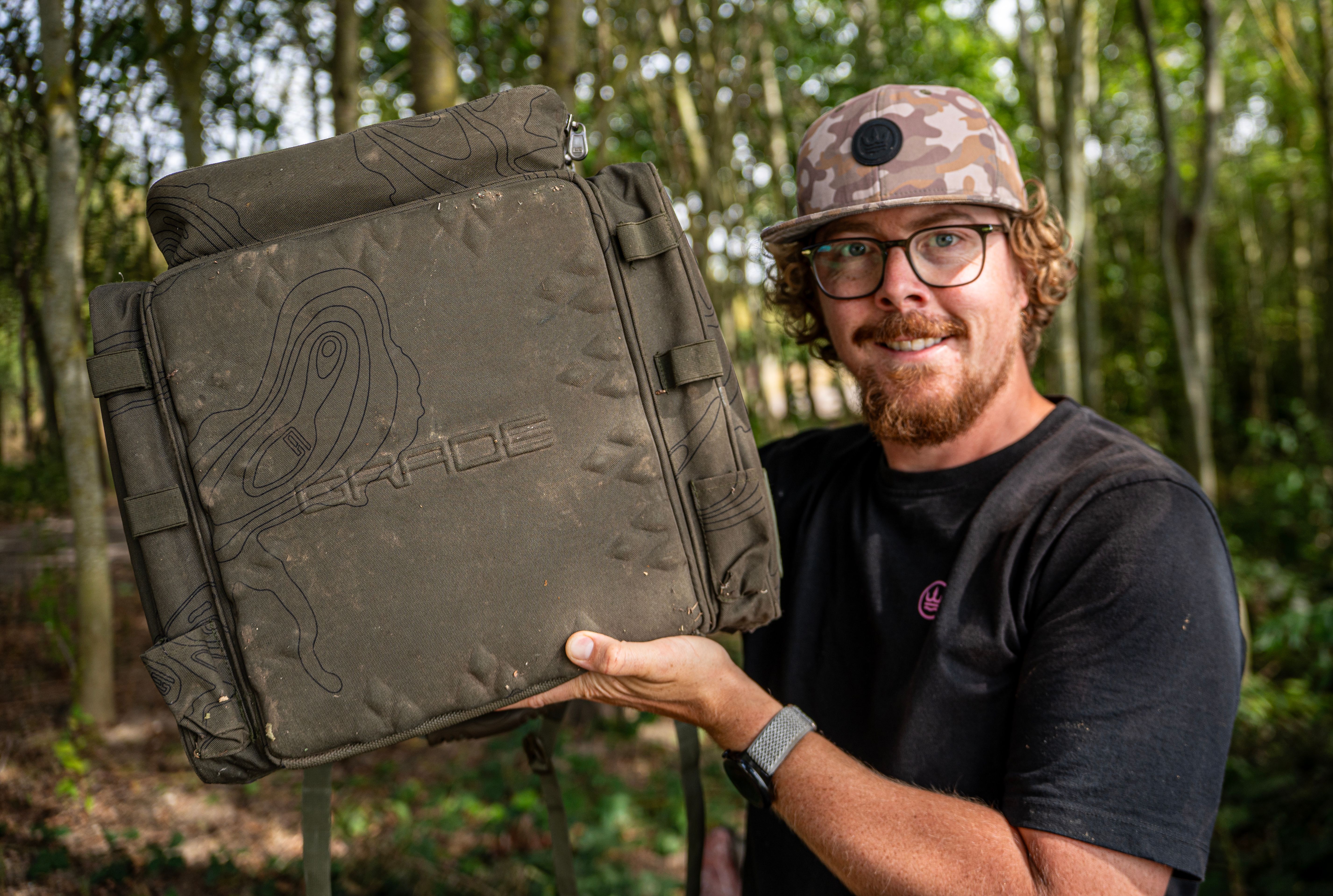 Heavy-duty olive green carp fishing rucksack sitting upright on bankside ground