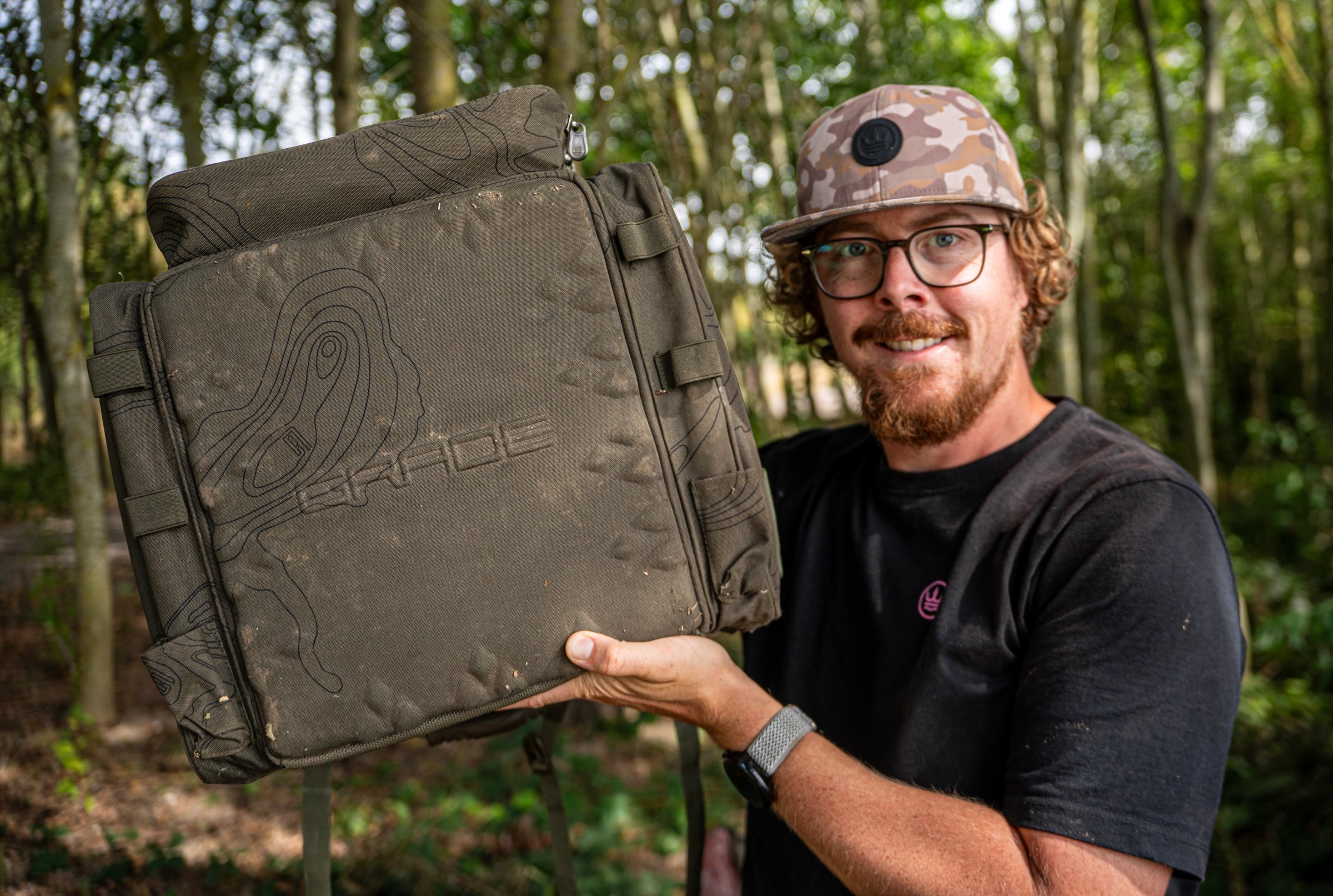Heavy-duty olive green carp fishing rucksack sitting upright on bankside ground