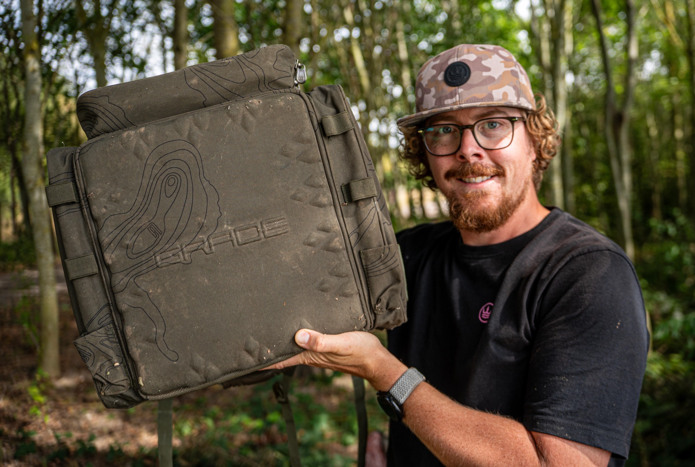 Heavy-duty olive green carp fishing rucksack sitting upright on bankside ground
