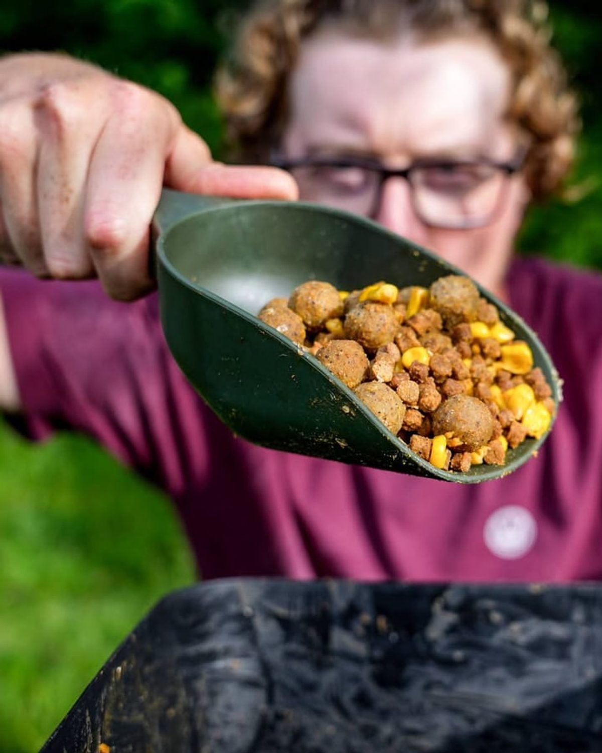 Joe holding out a scoop of boilies and sweetcorn over a bait bucket