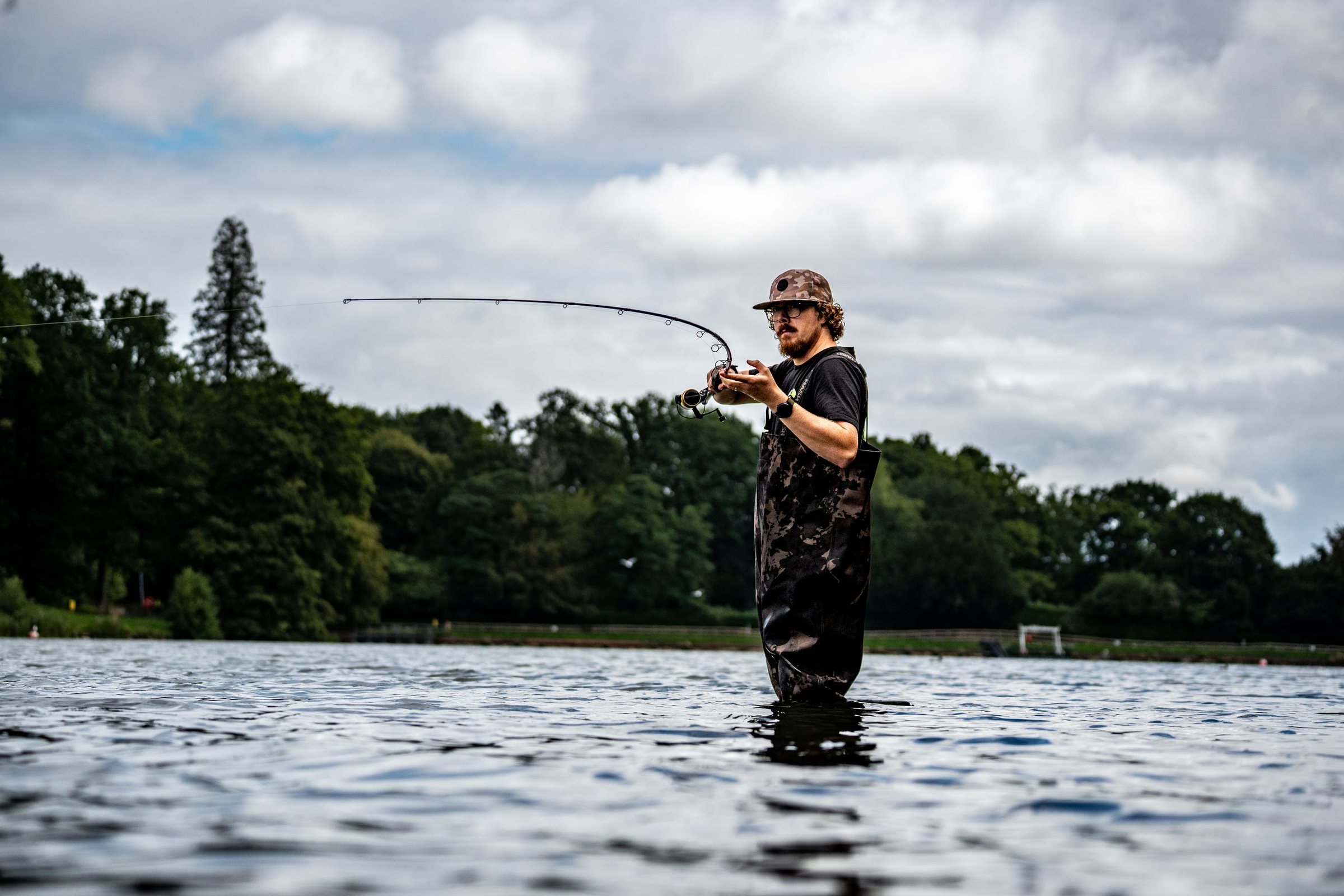 Joe Wooltorton wading a Somerset lake, mid-cast, rod bent against a cloudy sky