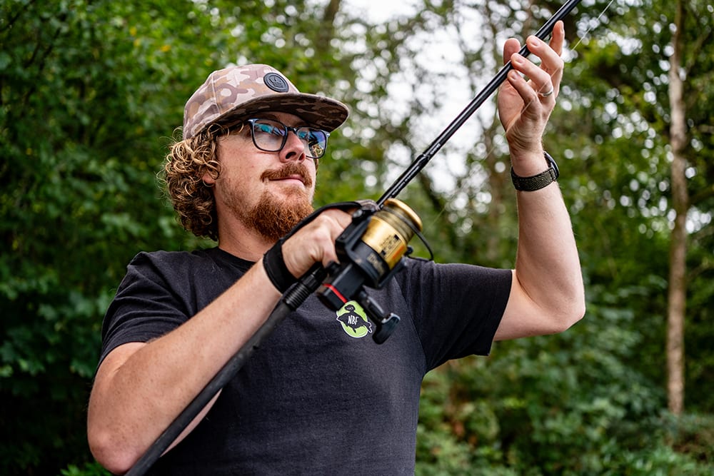 Joe checking his line with a rod raised, woodland behind him