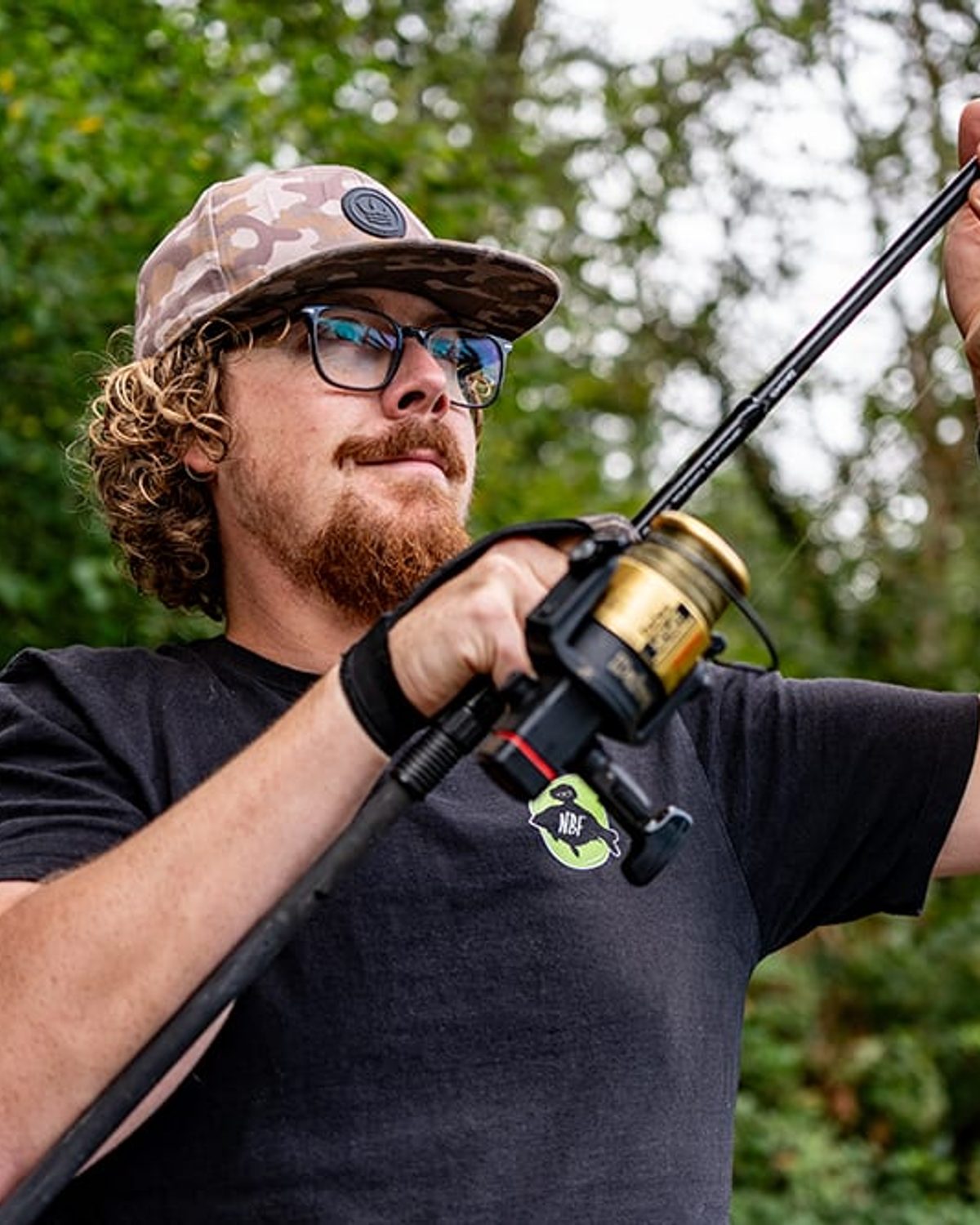 Joe checking his line with a rod raised, woodland behind him