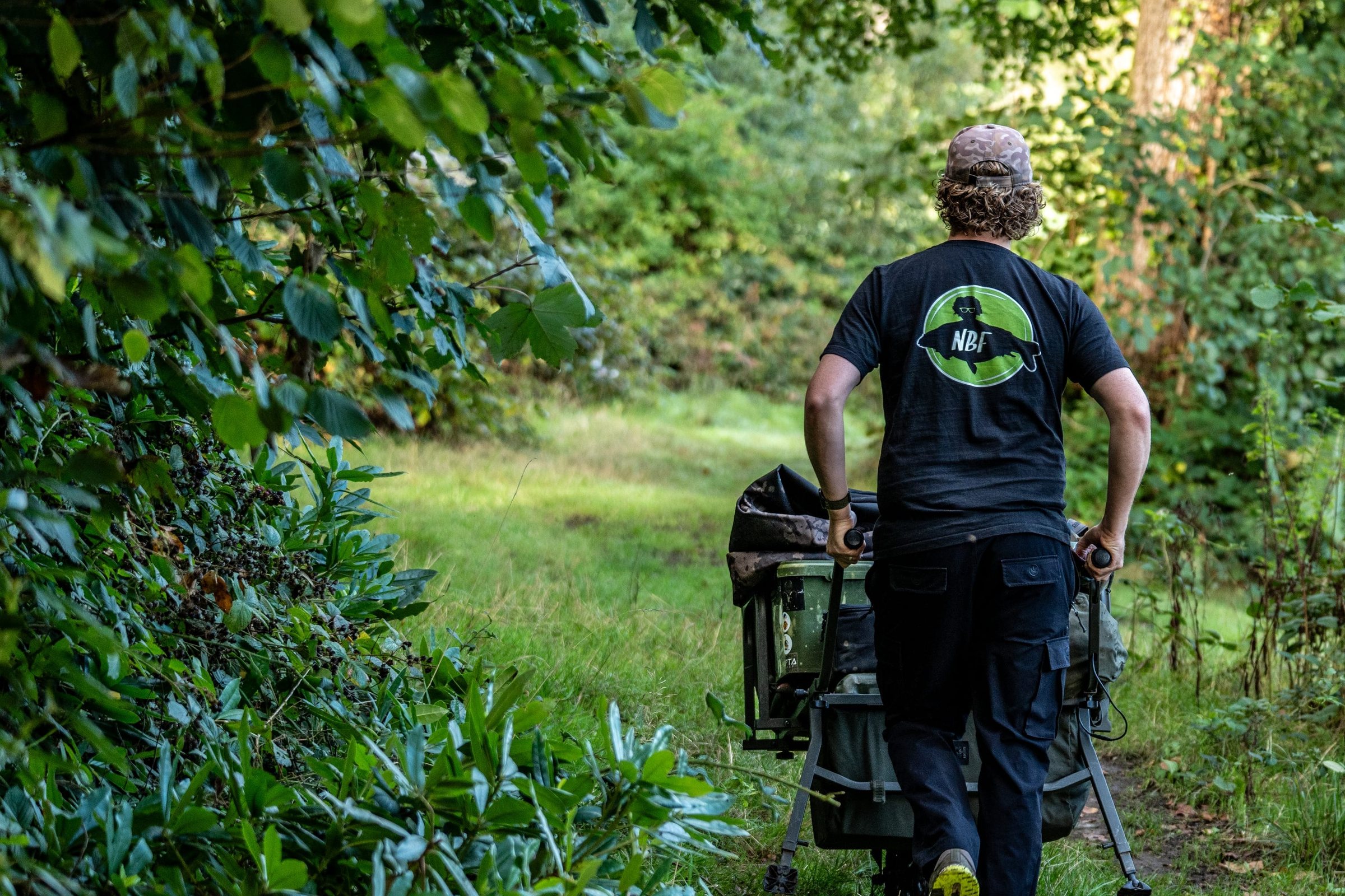 Joe pushing a loaded barrow along a woodland path to the lake