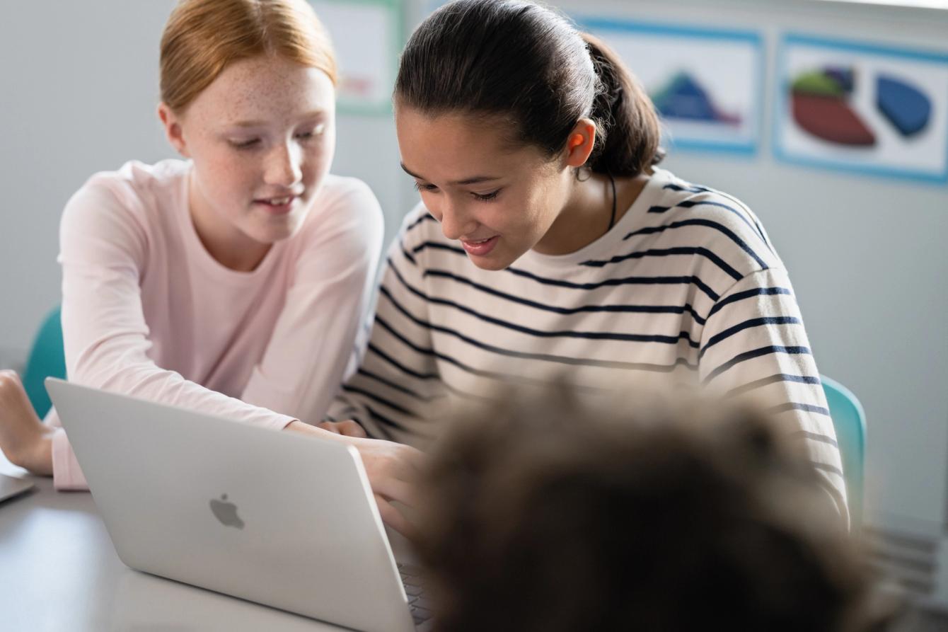 Deux adolescentes collaborent en regardant un ordinateur portable de la marque Apple dans une salle de classe