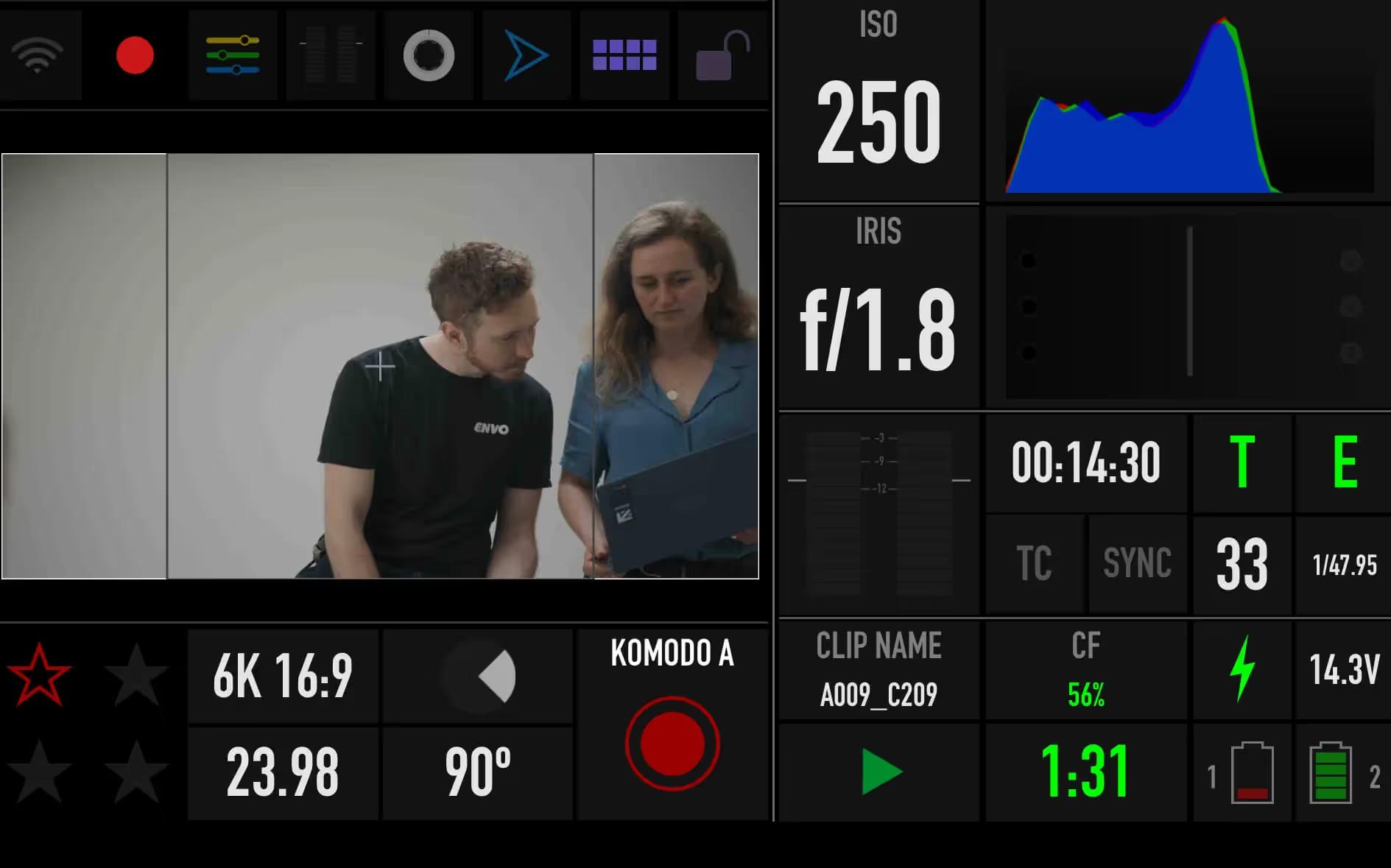Cinema camera monitor overlay showing ISO and aperture readouts around two people filming an interview