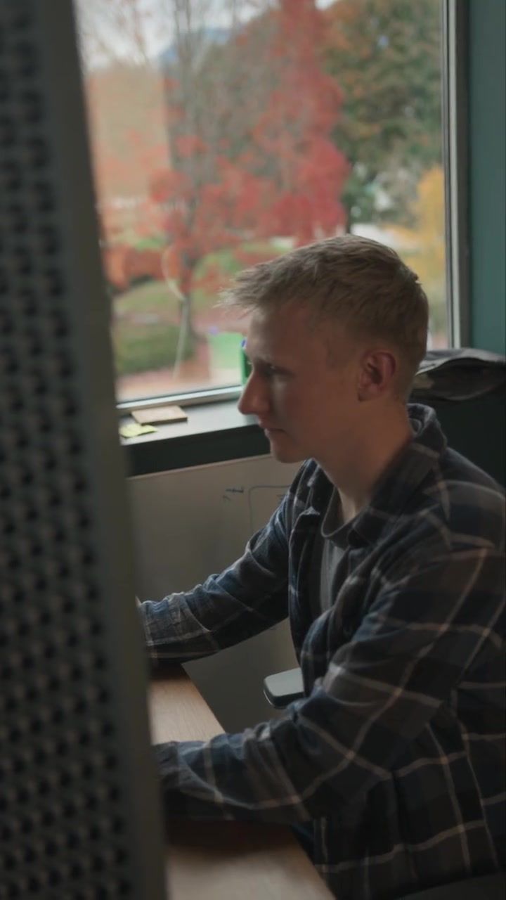 A man in a green shirt reaching towards a whiteboard mid-sentence, with three colleagues behind him listening, one holding a mug