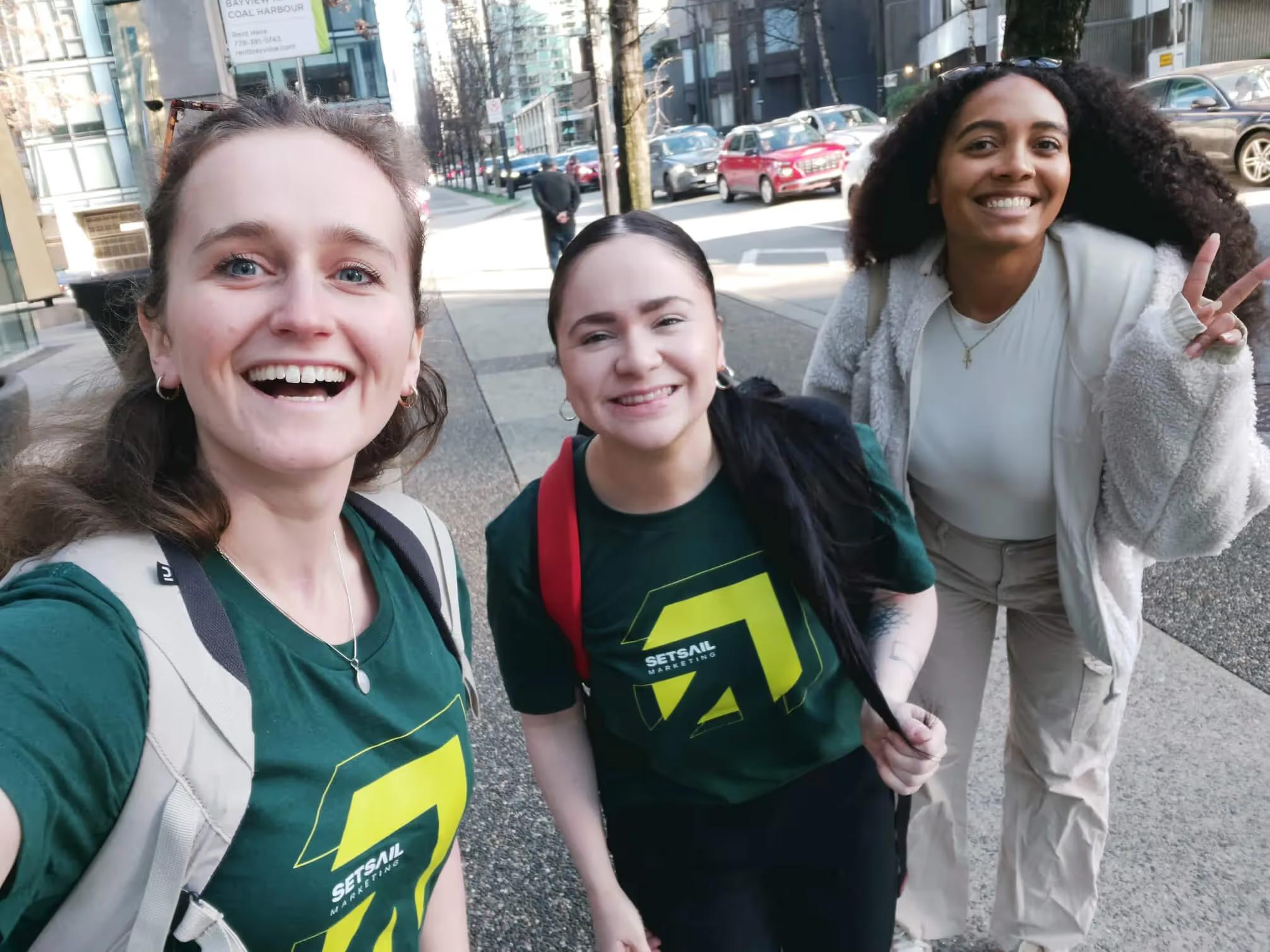 Three Setsail Marketing team members smiling in a street selfie, two wearing branded tees