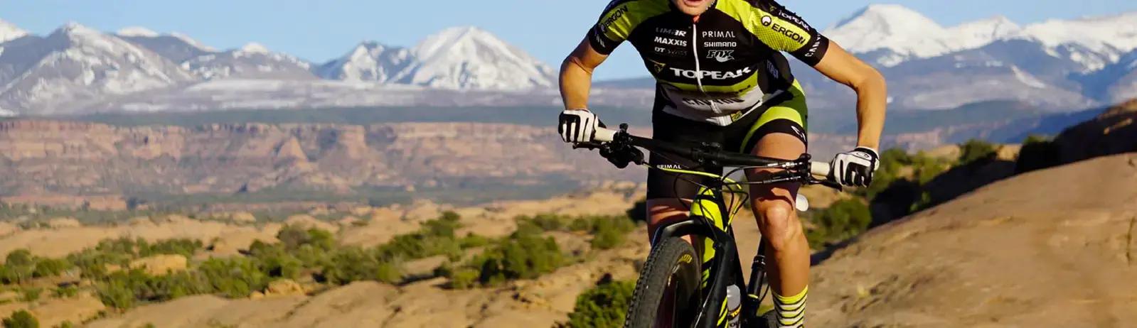 Mountain biker riding on trail with snow capped mountains in background