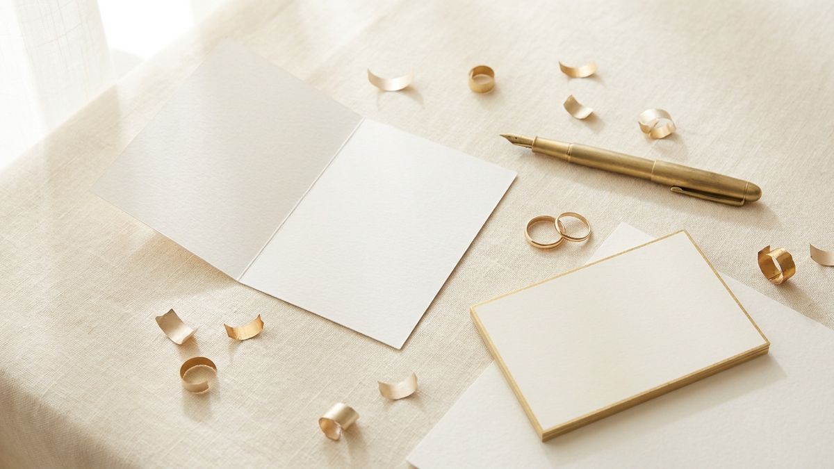 An editorial flat-lay of wedding prediction pool cards, a gold pen, and rings on cream stationery