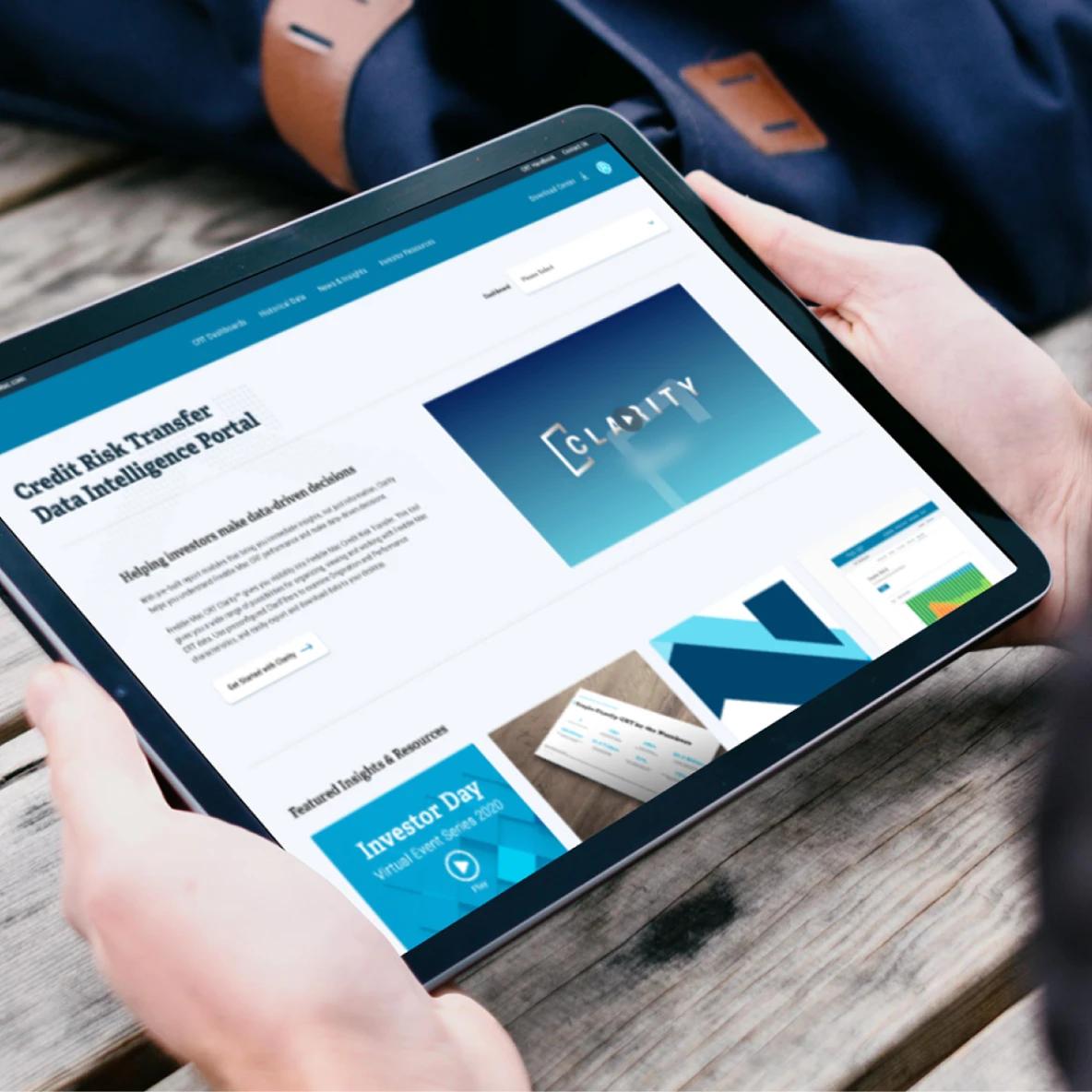 Person holding a tablet displaying the Credit Risk Transfer Data Intelligence Portal website, featuring the Claivity branding and information about helping innovators make data-driven decisions. The screen shows various data visualization elements and an Investor Day announcement.
