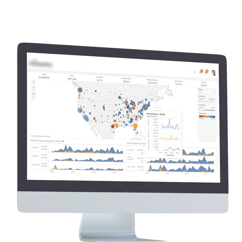 Computer monitor displaying a comprehensive business analytics dashboard with an interactive US map showing sales data points in blue and orange circles, multiple time-series graphs showing monthly sales trends, and a popup detail for Pennsylvania showing financial metrics and performance charts