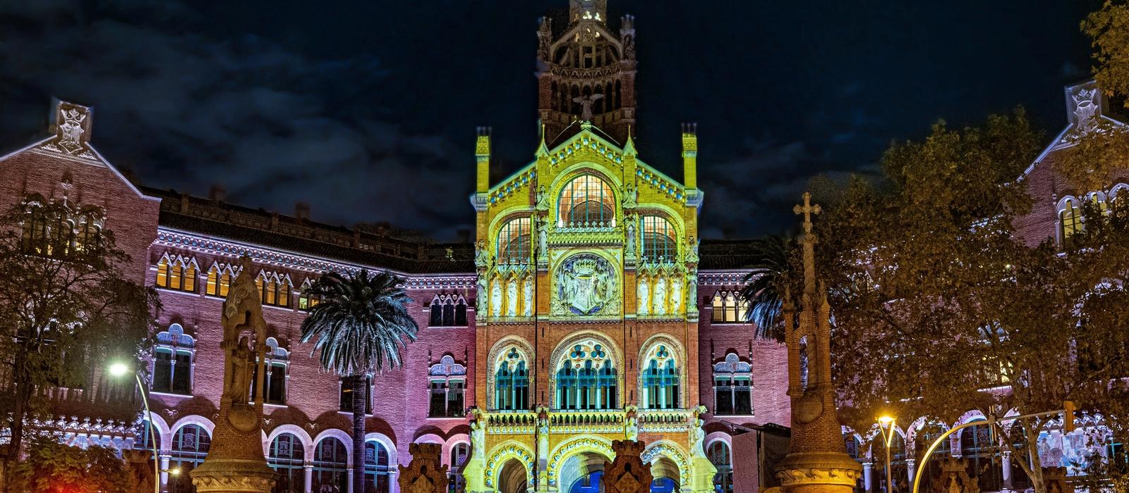 The ornate Modernista pavilions of Hospital de Sant Pau in Barcelona, with ceramic domes and sculpted facades set in peaceful gardens under a clear blue sky