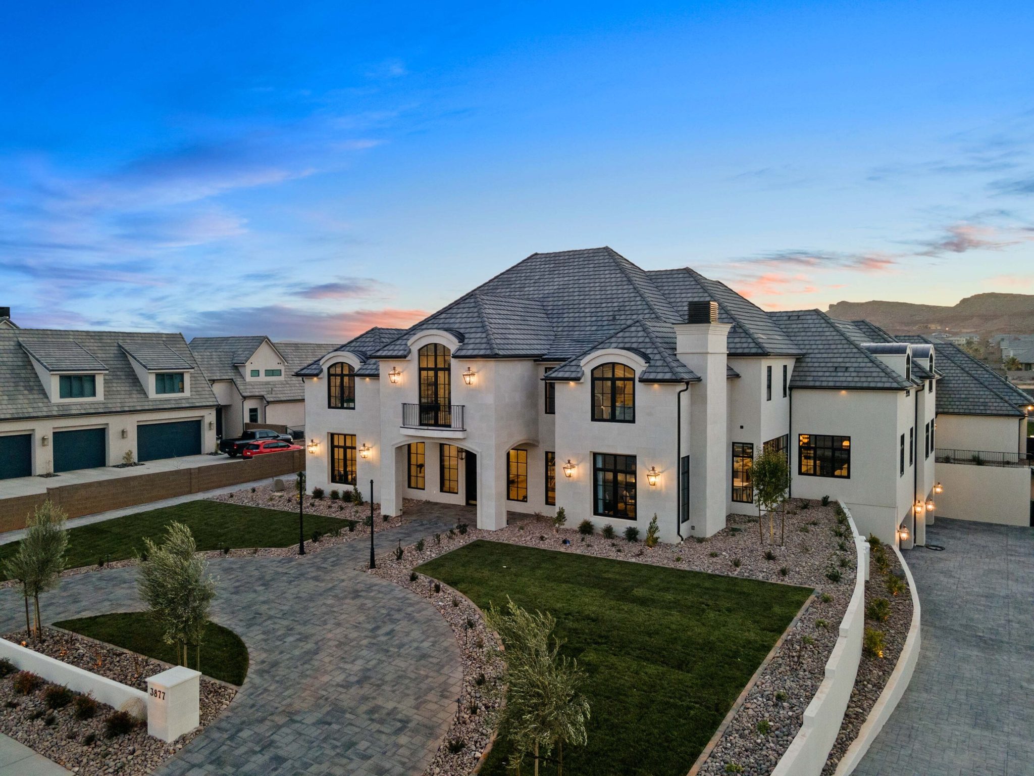 Large white custom home with a dark tile roof and a curved paver driveway, lit at dusk