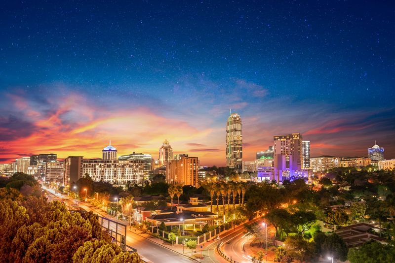 A brightly lit city skyline at sunset with modern high-rise buildings and a starry sky above