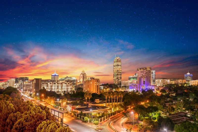 A brightly lit city skyline at sunset with modern high-rise buildings and a starry sky above
