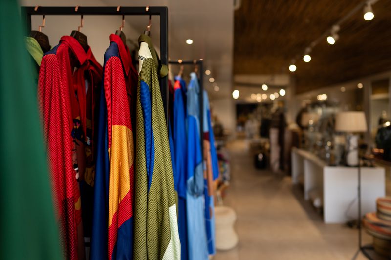 A colorful rack of garments is displayed in the boutique safari shop at Singita Kruger National Park, with the gallery's modern interior softly blurred in the background.
