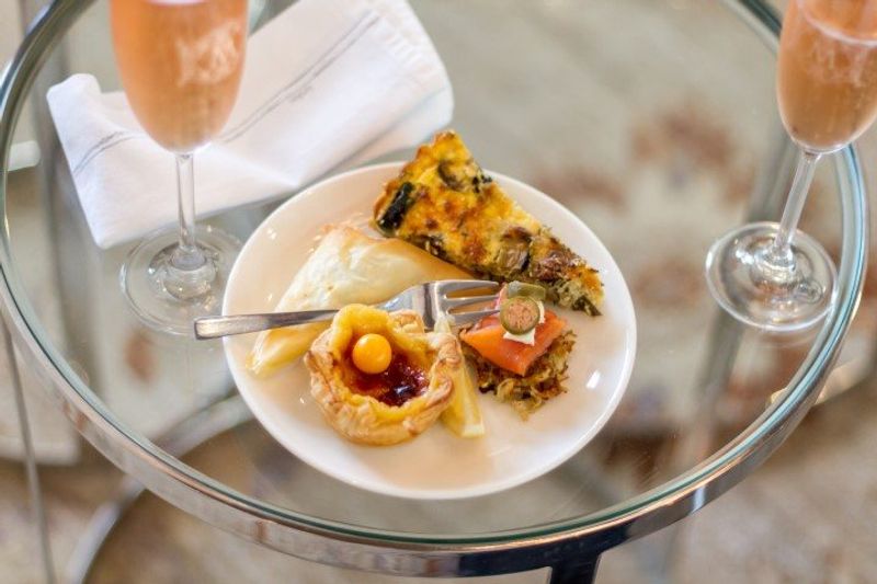 Leckere Häppchen auf einem Teller beim High Tea in MannaBay neben zwei Sektgläsern