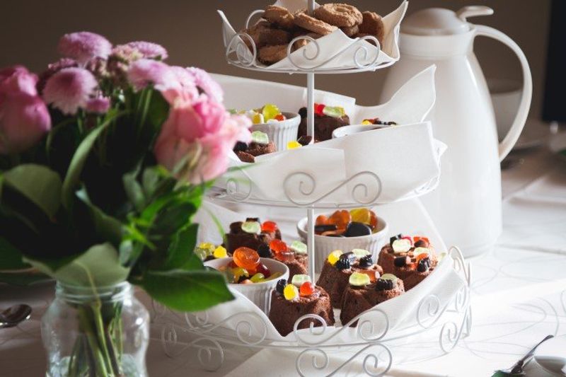 A tea table set with pink flowers, cakes, sweets and tea