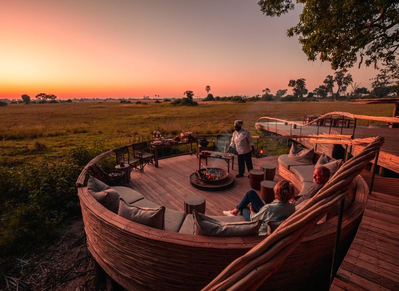 Guests relax around a firepit on a stylish deck overlooking the savannah at sunset, soaking in the magic of African travel in May.