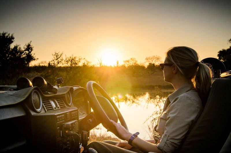 Jeune femme conduisant une voiture de safari au soleil levant dans la brousse.