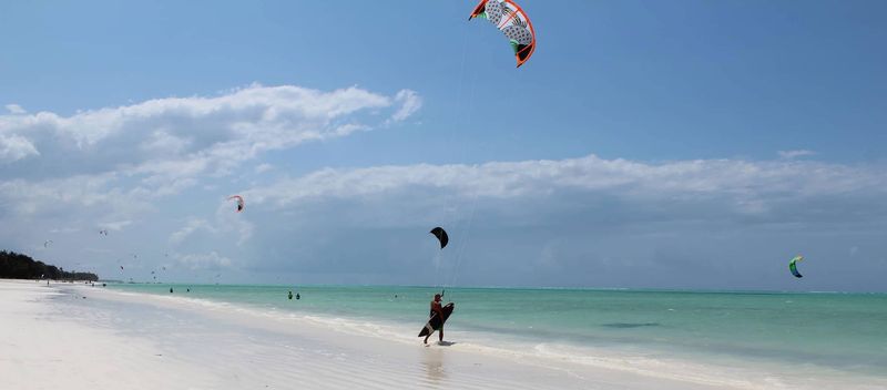 Ein Kitesurfer auf dem Ozean vorm weißen Sandstrand von Sansibar