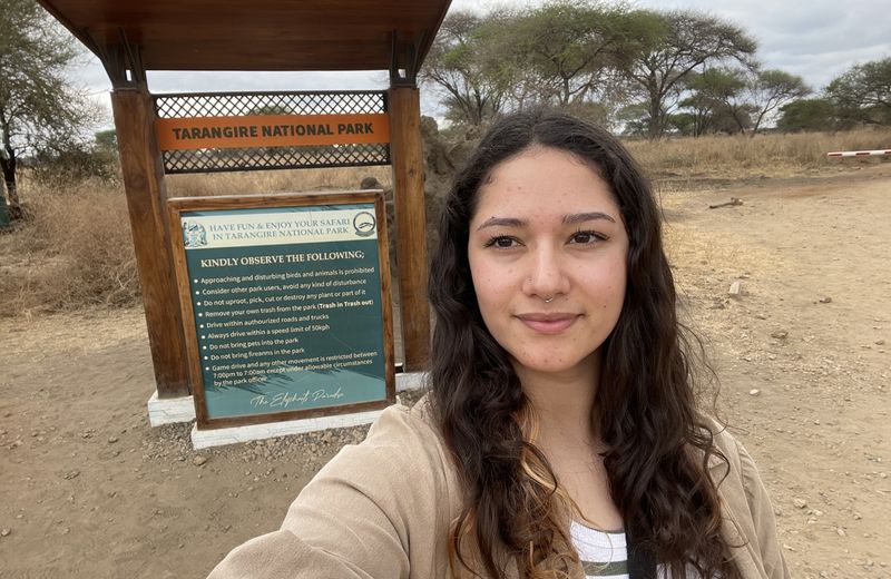 Rhino Africa Travel Expert Laura Hall stands in front of Tarangire National Park sign while on a Tanzania safari