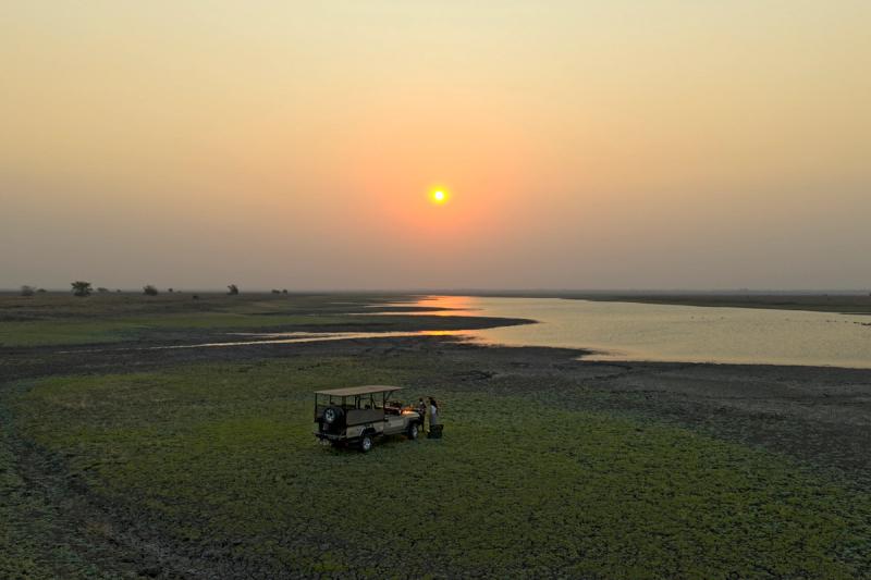 Safari vehicle beside a river and open floodplain at sunset in Gorongosa National Park, Mozambique.