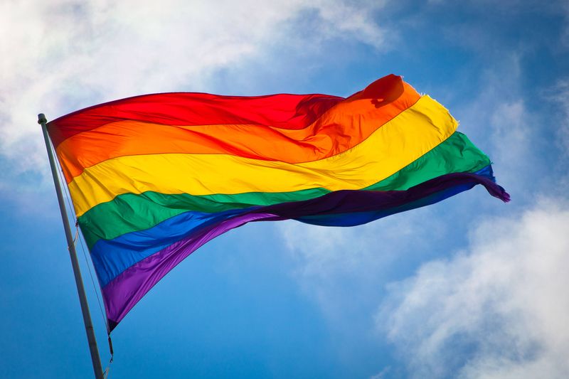 Die Regenbogenflagge weht im Wind vor blauem Himmel mit weißen Wolken