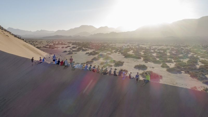 Drone shot of the group sitting on a sand dune