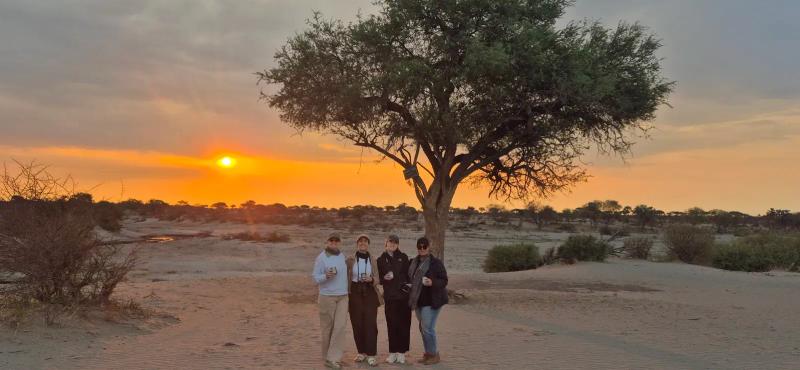 Four travellers enjoy a drink in front of a sunset in Botswana
