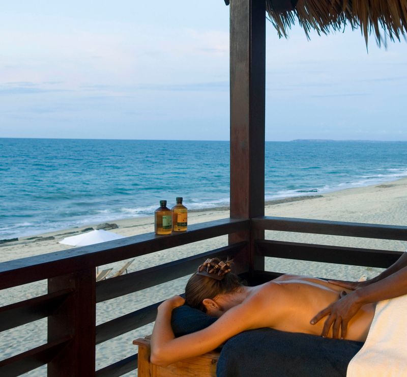 Eine Frau bekommt eine Massage auf einer Terrasse, daneben das Meer und Strand