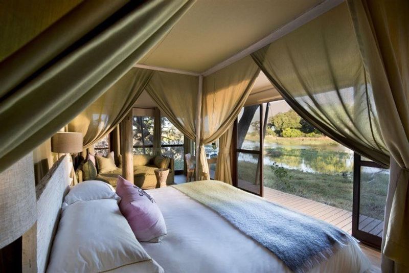 Frisch gemachtes Bett in einem offenen Zelt mit Blick auf eine Wasserlandschaft