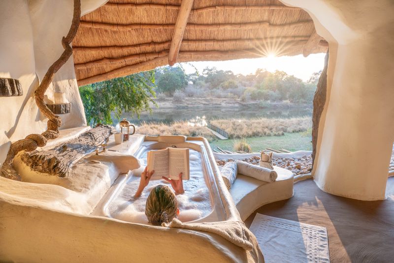 A woman reading a book, relaxing in a bathtub at Congwe Camp in Zambia