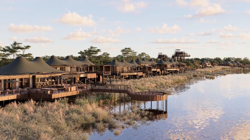 A line of elevated tented suites stretches along the riverbank, their canvas roofs glowing in soft light as part of one of the new luxury safari lodges 2026.