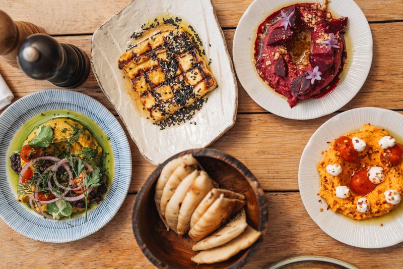 An array of small plates including pitas, grilled fish, salad, and colourful humus variations